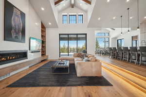 Living area with wood-type flooring, beam ceiling, high vaulted ceiling, a glass covered fireplace, and recessed lighting