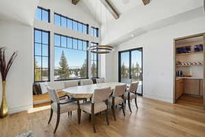 Dining space with beam ceiling, light wood-type flooring, a towering ceiling, and an inviting chandelier