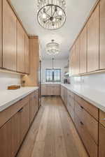 Kitchen with decorative light fixtures, light brown cabinetry, an inviting chandelier, and light wood-type flooring