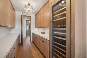 Kitchen featuring decorative light fixtures, light brown cabinets, wine cooler, a chandelier, and light hardwood / wood-style flooring