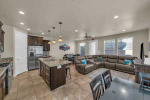 Kitchen with a breakfast bar, decorative backsplash, hanging light fixtures, an island with sink, and stainless steel appliances