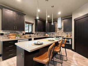 Kitchen featuring hanging light fixtures, light wood-type flooring, wall chimney exhaust hood, and a kitchen island