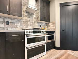 Kitchen with wall chimney exhaust hood, tasteful backsplash, double oven range, light wood-type flooring, and dark brown cabinets