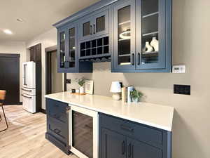 Kitchen featuring high end white refrigerator, wine cooler, blue cabinetry, and light hardwood / wood-style flooring