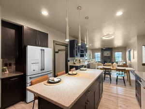 Kitchen featuring ceiling fan, decorative light fixtures, light wood-type flooring, white fridge with ice dispenser, and a kitchen island