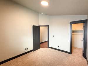 Unfurnished bedroom featuring a spacious closet, a closet, vaulted ceiling, and light colored carpet