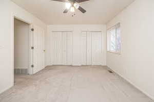 Unfurnished bedroom featuring ceiling fan, light colored carpet, and multiple closets