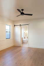 Unfurnished bedroom with ceiling fan, connected bathroom, hardwood / wood-style floors, and a barn door