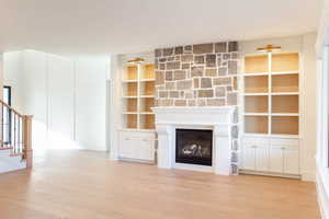 Unfurnished living room featuring a large fireplace, built in shelves, and light wood-type flooring