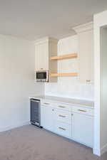 Kitchen with tasteful backsplash, white cabinets, light carpet, and wine cooler