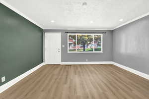 Empty room with a textured ceiling, ornamental molding, and light wood-type flooring