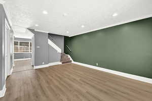 Unfurnished living room featuring a textured ceiling, crown molding, and hardwood / wood-style floors