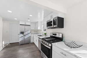 Kitchen with sink, dark wood-type flooring, appliances with stainless steel finishes, white cabinets, and light stone counters