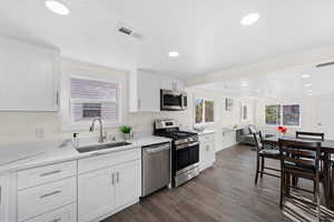 Kitchen featuring light stone countertops, white cabinets, appliances with stainless steel finishes, dark hardwood / wood-style flooring, and sink