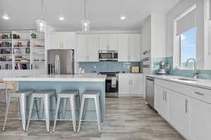 Kitchen with an island, sink, white cabinetry, and stainless steel appliances