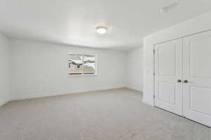 Unfurnished bedroom featuring light colored carpet, a closet, and a textured ceiling