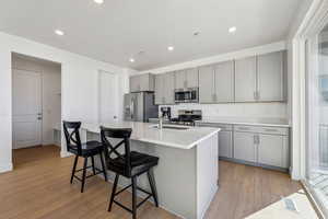 Kitchen featuring a breakfast bar, light hardwood / wood-style flooring, a kitchen island with sink, gray cabinetry, and stainless steel appliances