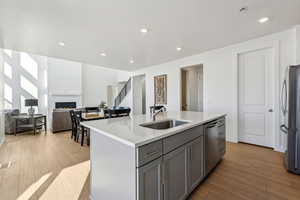 Kitchen featuring appliances with stainless steel finishes, gray cabinetry, light hardwood / wood-style floors, sink, and a center island with sink