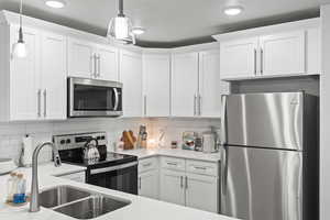 Kitchen with decorative backsplash, pendant lighting, stainless steel appliances, and white cabinetry