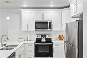 Kitchen featuring sink, white cabinetry, appliances with stainless steel finishes, and hanging light fixtures