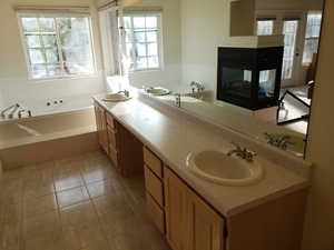 Bathroom with tile patterned flooring, a multi sided fireplace, tiled tub, and vanity