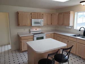 Kitchen featuring light brown cabinetry, sink, white appliances, and a kitchen island