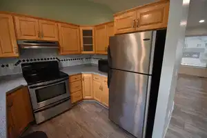 Kitchen featuring light wood-type flooring, backsplash, vaulted ceiling, and appliances with stainless steel finishes