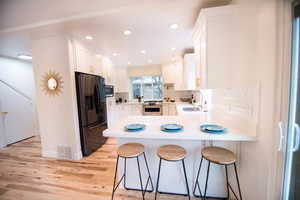 Kitchen featuring white cabinetry, kitchen peninsula, appliances with stainless steel finishes, a kitchen breakfast bar, and sink