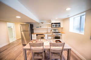 Kitchen with light hardwood / wood-style floors, sink, appliances with stainless steel finishes, a breakfast bar area, and white cabinets