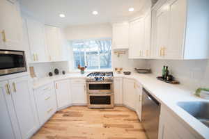 Kitchen featuring decorative backsplash, appliances with stainless steel finishes, white cabinetry, and hardwood floors