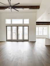 Spare room featuring ceiling fan with notable chandelier, hardwood / wood-style floors, beamed ceiling, and french doors