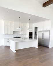 Kitchen featuring white cabinetry, stainless steel appliances, a kitchen island with sink, pendant lighting, and beamed ceiling