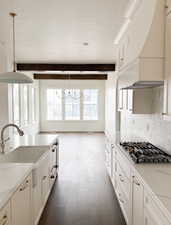 Kitchen with custom exhaust hood, white cabinets, hanging light fixtures, and beamed ceiling