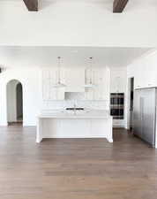 Kitchen featuring appliances with stainless steel finishes, pendant lighting, white cabinets, and an island with sink