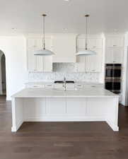 Kitchen featuring hanging light fixtures, a kitchen island with sink, stainless steel appliances, and white cabinetry