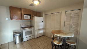 Kitchen featuring white appliances, a textured ceiling, and light tile patterned floors