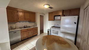 Kitchen featuring white appliances, a textured ceiling, light tile patterned floors, and sink