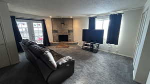 Carpeted living room featuring a fireplace, a textured ceiling, and french doors