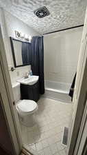 Full bathroom with toilet, a textured ceiling, backsplash, shower / tub combo, and vanity