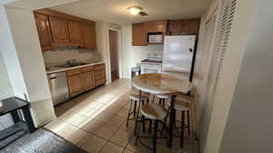 Kitchen with sink, white appliances, a textured ceiling, and light tile patterned flooring