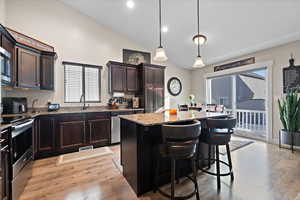 Kitchen featuring decorative light fixtures, light hardwood / wood-style floors, a center island, a breakfast bar area, and stainless steel appliances