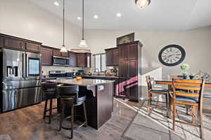 Kitchen with light stone countertops, appliances with stainless steel finishes, a kitchen island, decorative light fixtures, and dark hardwood / wood-style floors