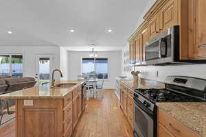 Kitchen featuring stainless steel appliances, a kitchen island with sink, light wood-type flooring, a notable chandelier, and sink