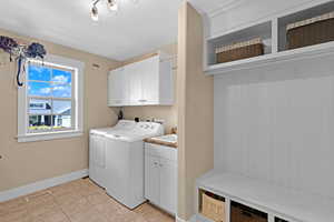 Laundry area featuring light tile patterned floors, washing machine and clothes dryer, and cabinets