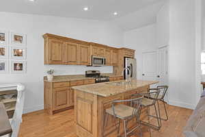 Kitchen featuring light stone countertops, stainless steel appliances, sink, a kitchen breakfast bar, and a center island with sink