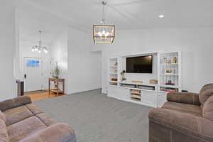 Living room with built in shelves, vaulted ceiling, a chandelier, and carpet flooring