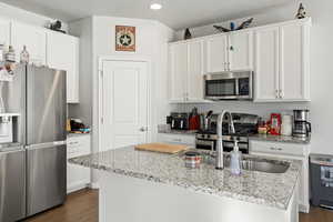 Kitchen with white cabinets, a kitchen island with sink, appliances with stainless steel finishes, and light stone counters