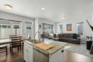 Kitchen featuring a textured ceiling, white cabinets, dishwasher, sink, and a kitchen island with sink