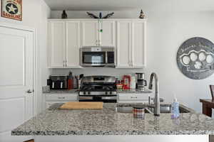 Kitchen with white cabinetry, appliances with stainless steel finishes, a kitchen island with sink, light stone counters, and sink