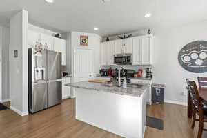 Kitchen with white cabinetry, a center island with sink, appliances with stainless steel finishes, light stone countertops, and sink